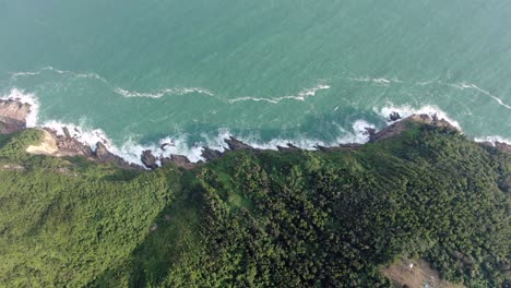 Aerial-view-of-a-jagged-rock-island,-surrounded-with-lush-green-nature-and-Hong-Kong-bay-water