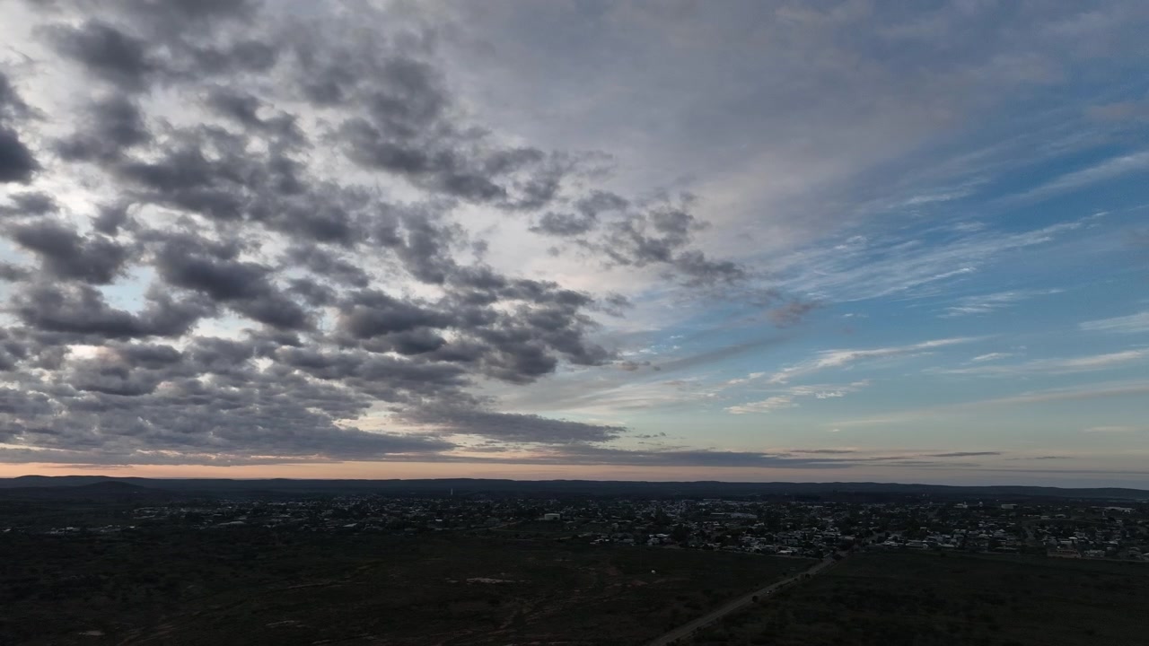 Ampia veduta aerea su Broken Hill che mostra la transizione da dense nuvole all'alba a un cielo mattutino limpido e azzurro sopra la città e il paesaggio semi-arido circostante.