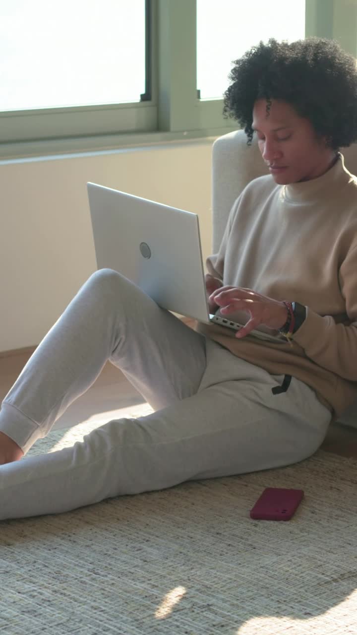 Vertical video: Typing with laptop open at home, man in top shifting and working, pink phone near