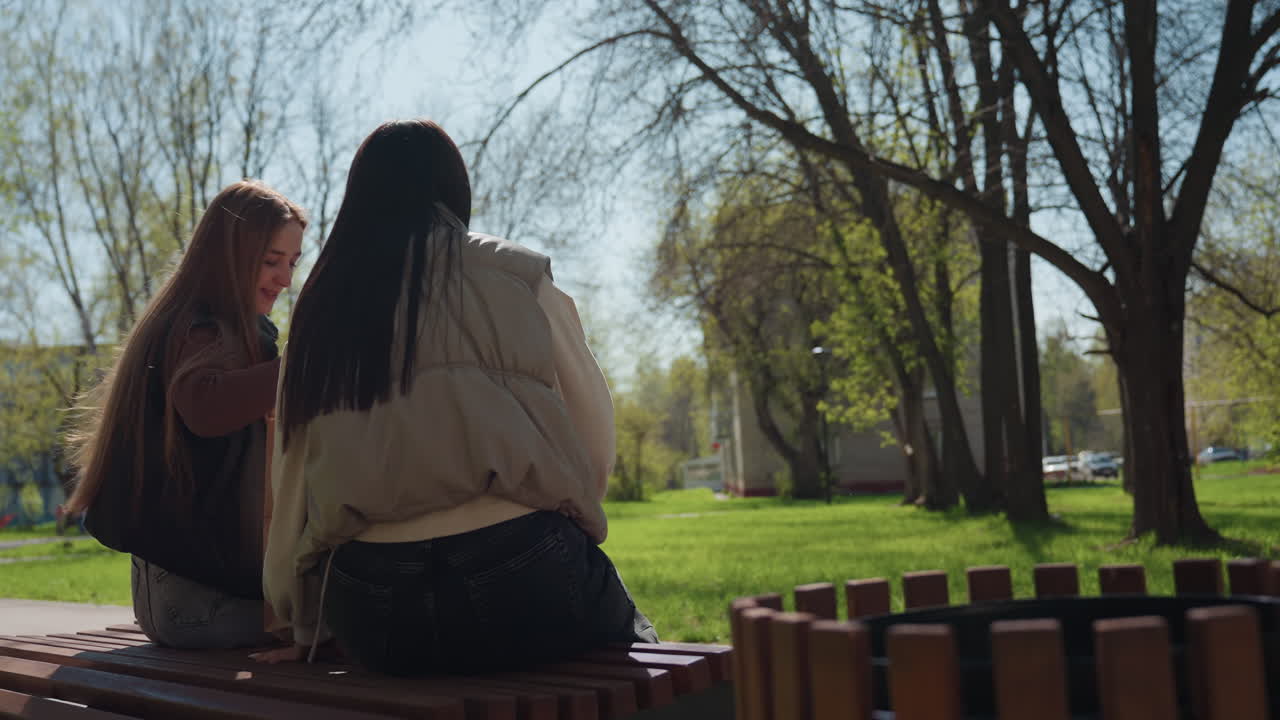 공원에서 휴식을 취하는 여성들, 공원 벤치에 앉아 있는 두 여성, 아시아 여성과 백인 여성이 야외에서 즐거운 시간을 함께 보내고 있습니다. 서로 다른 배경을 가진 젊은 여성들이 활기찬 봄 공원에서 함께 웃고 있네요.