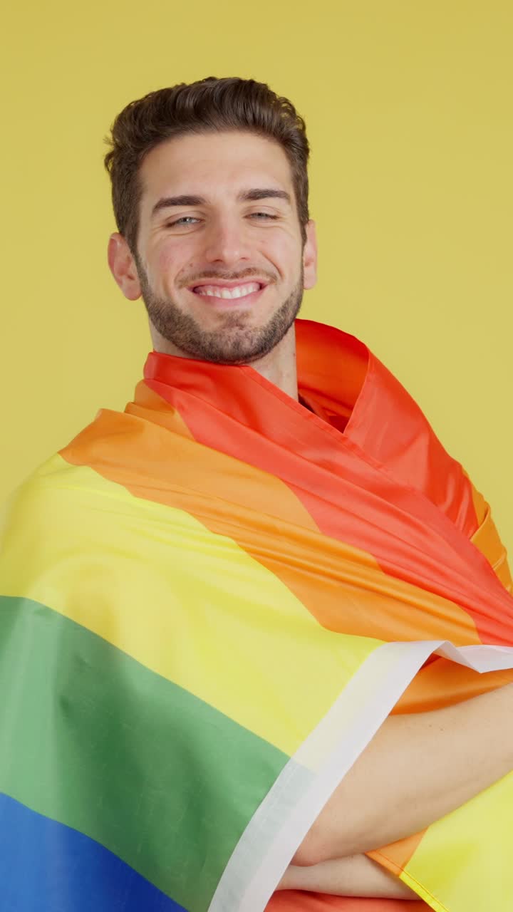 Smiling man wrapped in LGBTQ+ rainbow flag