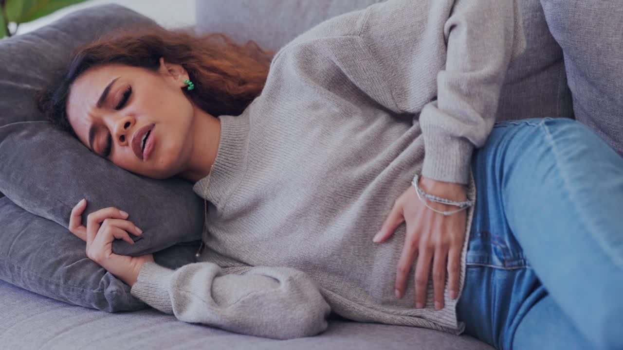 Person, sick and period pain on home sofa