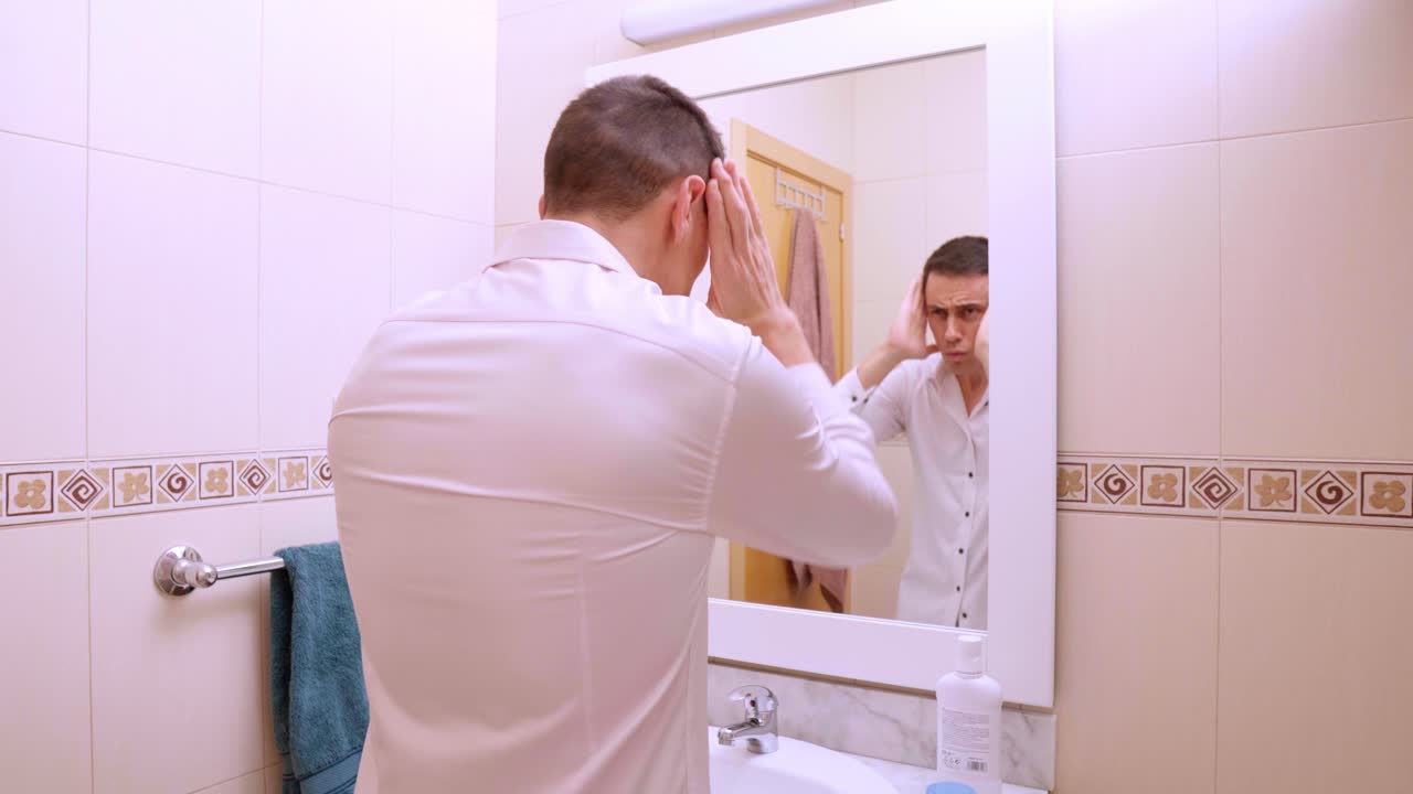 Narcissistic man combing hair and admiring himself in bathroom mirror