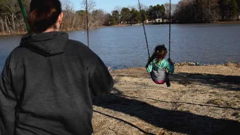 Mother-pushing-a-young-daughter-on-a-swingset-at-a-park-at-the-lake