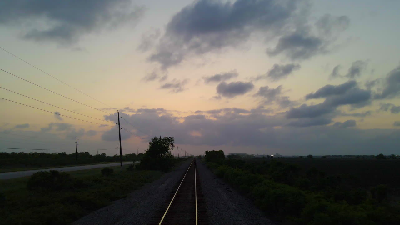 Drone Shot Following Railroad Track In Texas, U.S.A., Before Lifting Up And Over Track And Country Road After Sunset