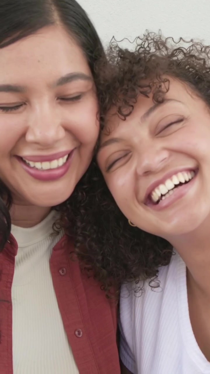 Video vertical: Mujer inclinándose, dos mujeres compartiendo alegría en el sofá con top blanco, reloj inteligente visible.