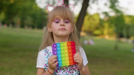 Child-kid-play-with-pop-it-sensory-toy,-girl-presses-on-squishy-silicone-touch-screen-bubbles