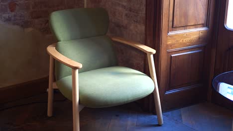 green armchair with wooden arms in a room with a brick wall