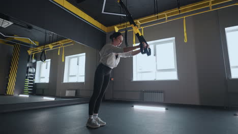 doing trx exercises. young athletic woman in sports clothing training legs with trx fitness straps in the gym. exercise where stabilizing muscles trained and the whole body is working truly functional