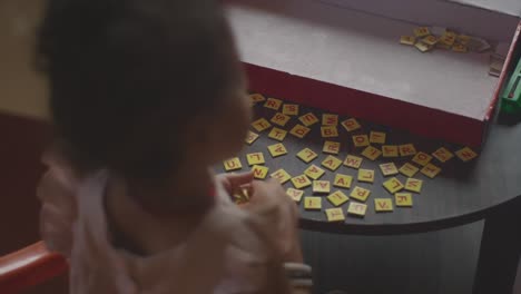 static handheld shot from above of a playing little girl playing a game with letters while putting together different words