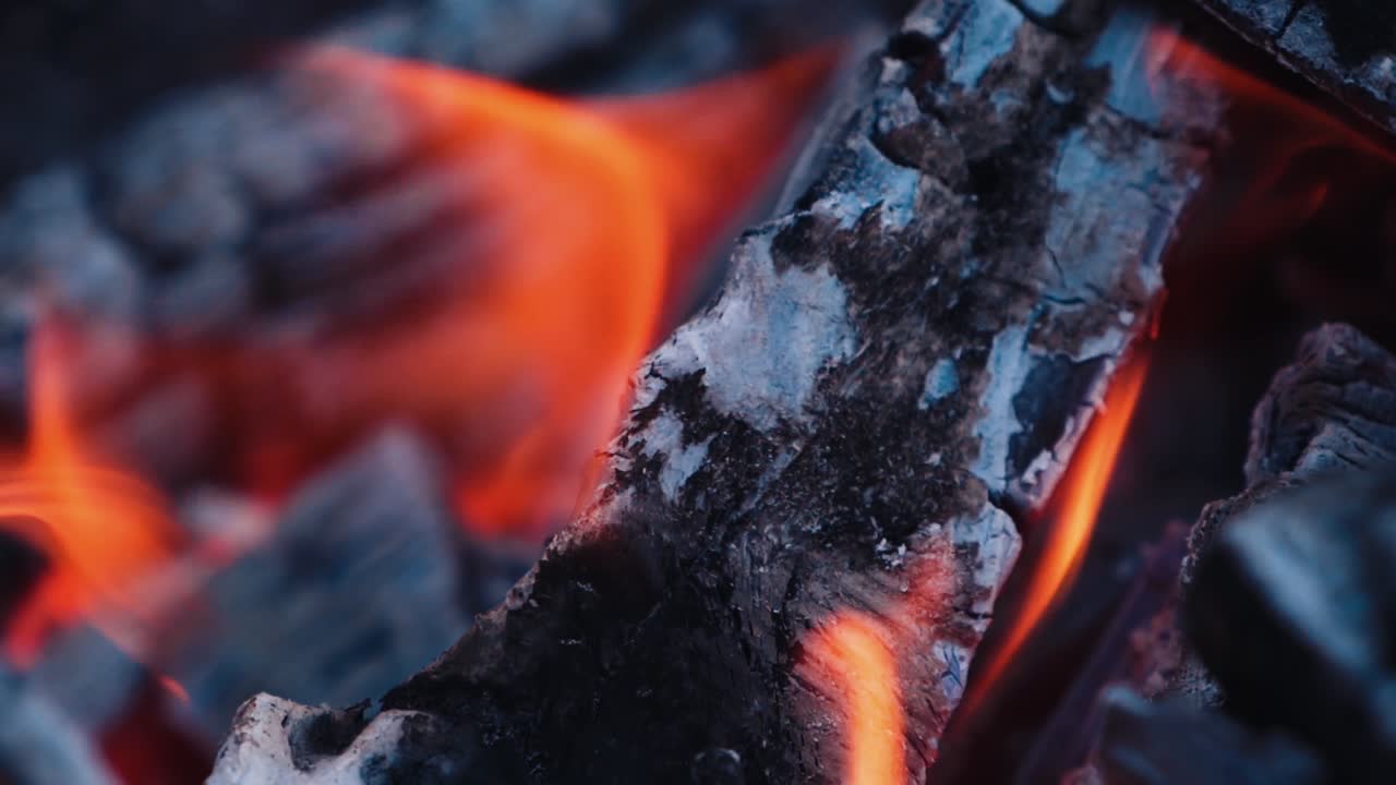 Wood burning with ash. Close-up shot of wood and charcoal with slight orange flame. Slow motion.
