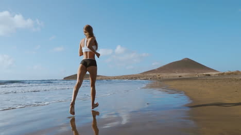 fitness runner woman running on beach listening to music motivation with phone case sport armband strap. sporty athlete training cardio barefoot with determination under summer sun.