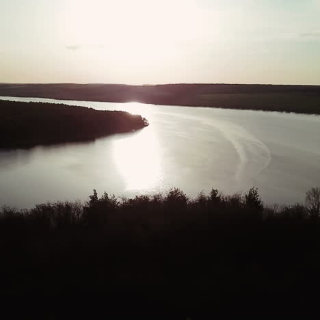wide and quiet river is located between the fields and forests at sunrise. a small house stands on the bank of the river with a beautiful view of the countryside. aerial view.