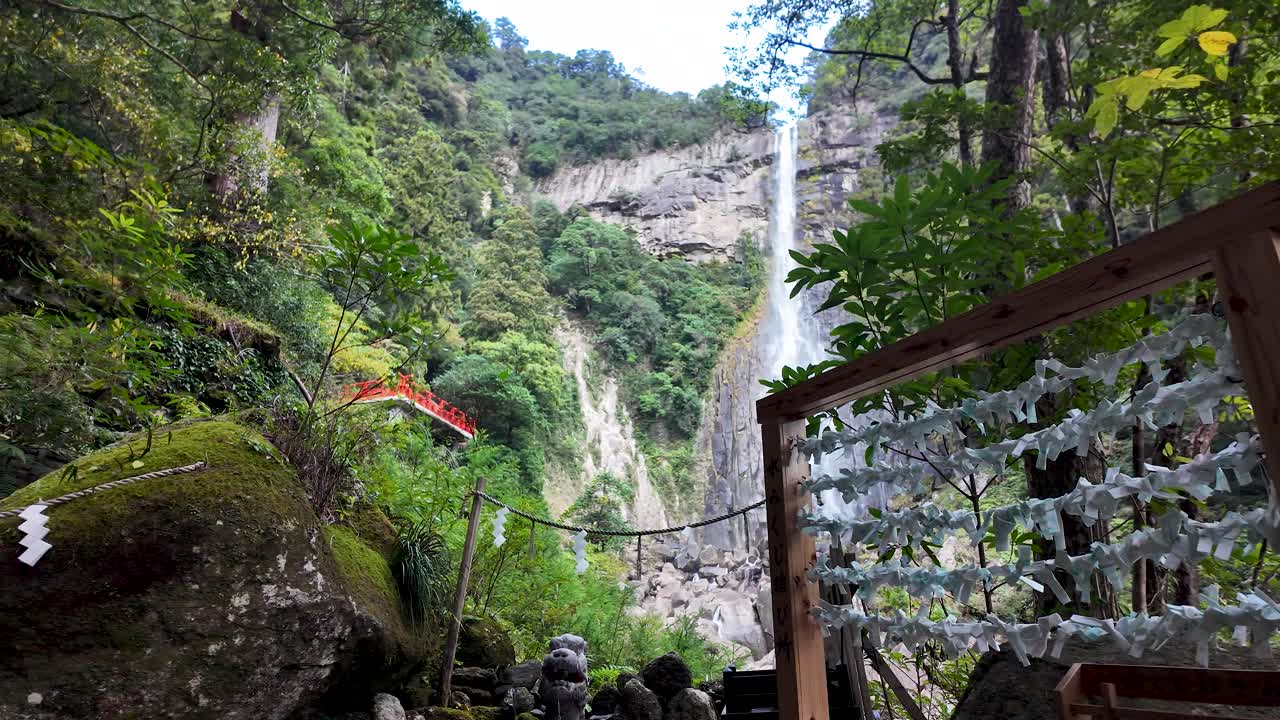 Omikuji fortune telling paper strips hanging near Nachi waterfall with a red bridge in the background, Nachi Katsuura, Japan