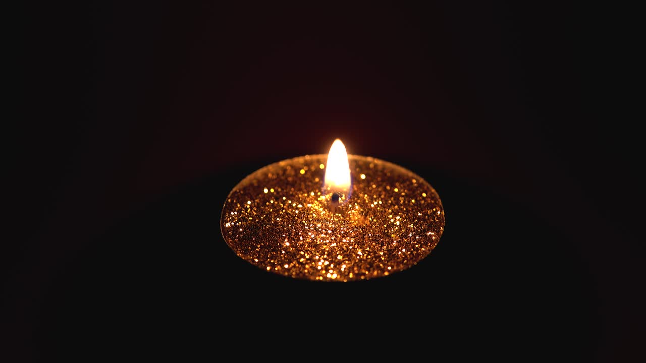 Candela dorata con bellissime scintille accesa su uno sfondo rosso scuro.