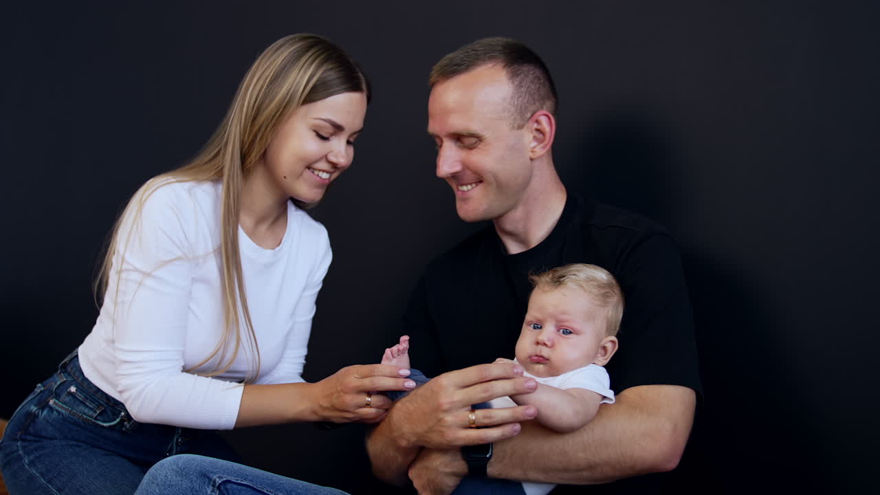Loving young couple with their adorable baby. Mom kisses tiny foot of her baby and man kisses his wife on the head.