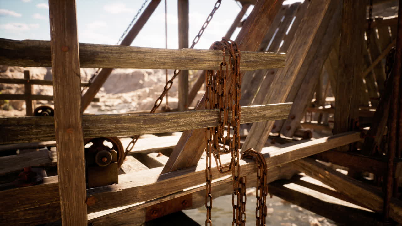 Rusty chains hanging from a wooden structure over water in bright sunlight
