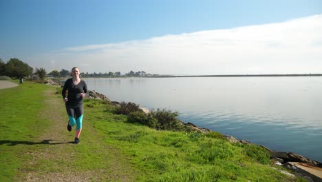 runner on alameda island running on the shoreline of the san francisco bay wearing colorful teal leggings and dark top.