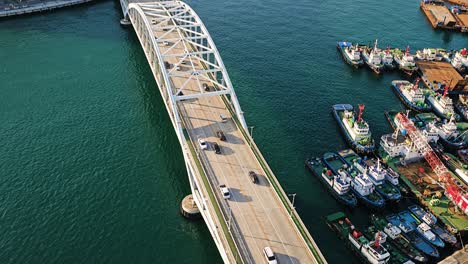 drone view of busan bridge in south korea showing vehicles crossing above blue waters with moored ships alongside the harbor