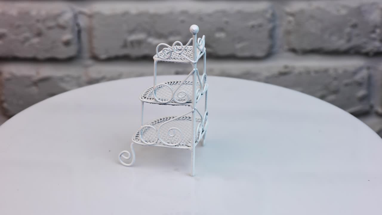 Beautiful ornamented shelf-stand rotating at the table. Toy furniture item for doll's house at the backdrop of white brick wall.