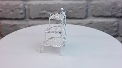 beautiful ornamented shelf-stand rotating at the table. toy furniture item for doll's house at the backdrop of white brick wall.