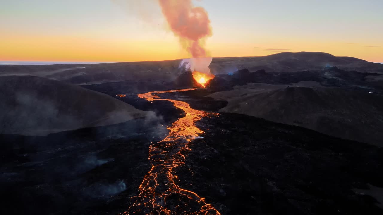 Ripresa aerea con drone di un vulcano attivo al tramonto, che mostra un fiume di lava incandescente scorrere attraverso il paesaggio con una calda luce serale nel cielo.
