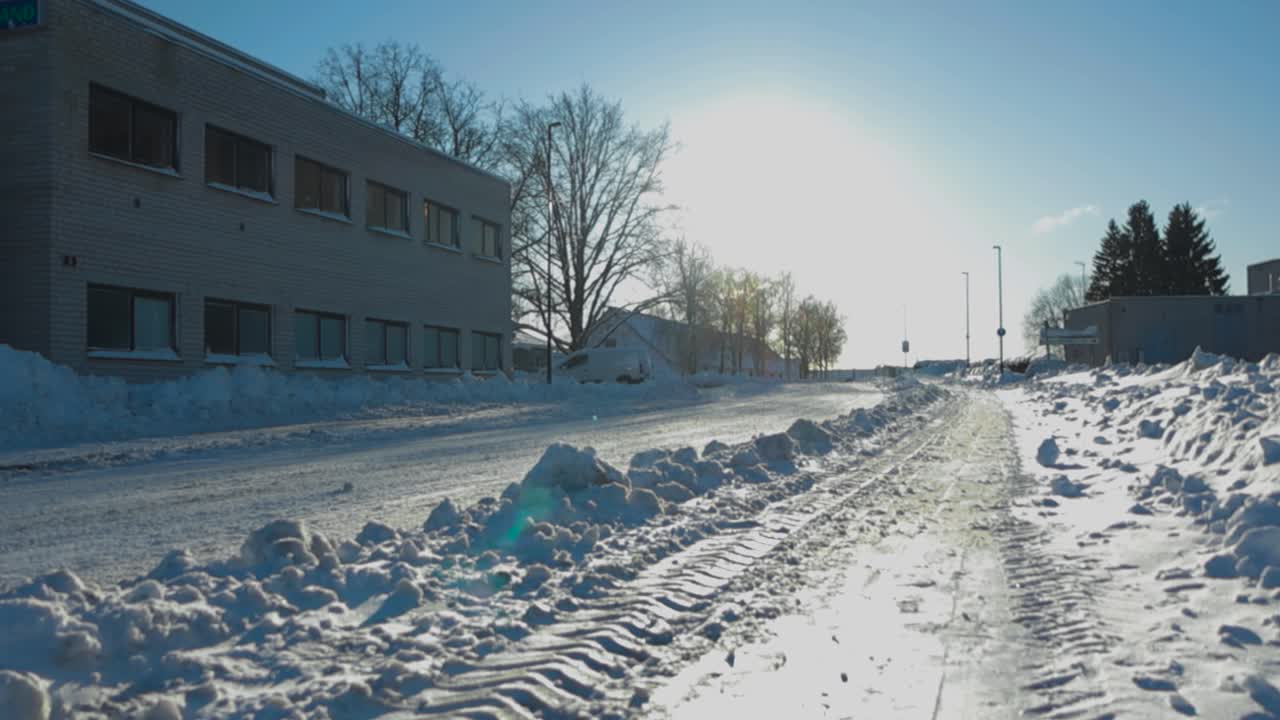Gorgeous low angle footage of a lonely street covered in thick white and fluffy snow during a winter sunny day with sun creating sun rays and lense flare in the footage. Old brick building and road.