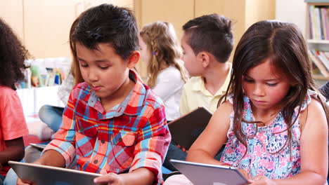 elementary school pupils sitting on floor using tablets