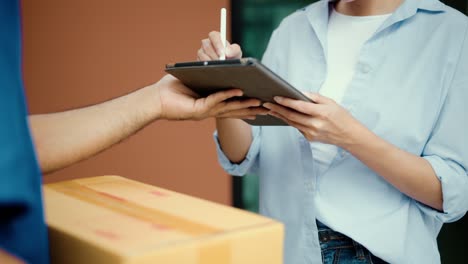 hand woman signing electronic signature on tablet for agreement of contract digital receiving parcel from blue delivery man from shopping online. courier man delivering package to destination.