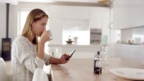 mujer real usando teléfono móvil en casa bebiendo café disfrutando de un estilo de vida relajante