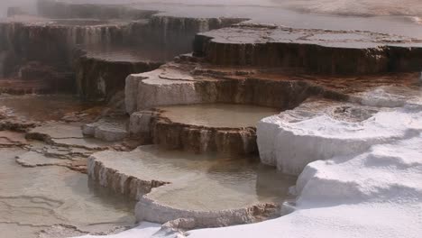 a colorful closeup look at a hot springs limestone terrace with steam snow and thermal pool