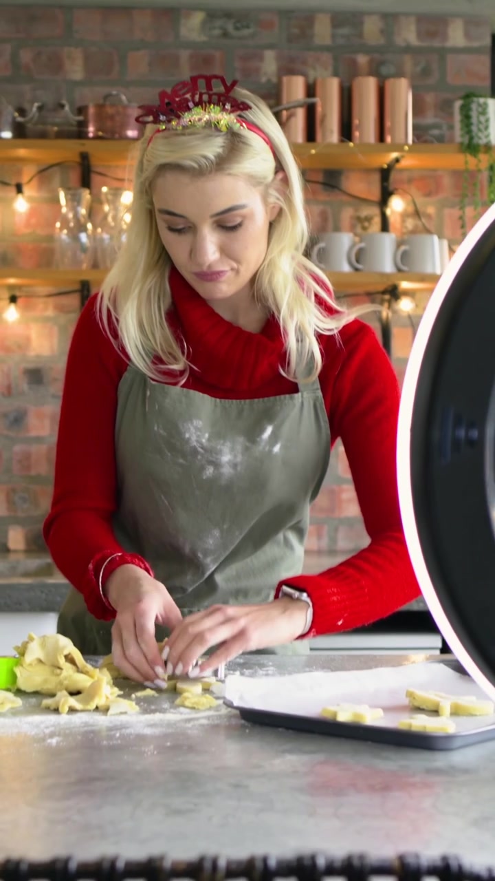 Video verticale: Donna in grembiule che taglia l'impasto con un taglierino sul bancone, ring light che riprende con il telefono.