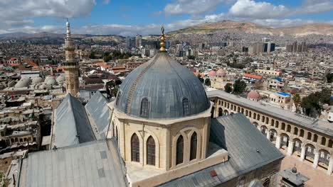 aerial view of the top ot the umayyad mosque in syria. drone is flying over the mosque with the city of damascus in the background.