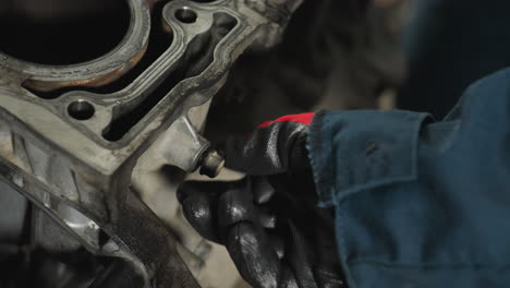 close-up of hand in red glove tightening nut on block engine, showcasing precision and mechanical expertise in automotive workshop, emphasizing detailed repair and maintenance work