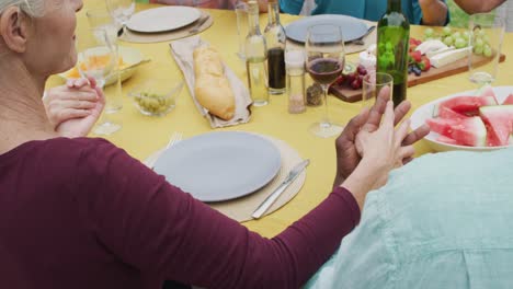 animation of happy diverse female and male senior friends having lunch in garden, praying