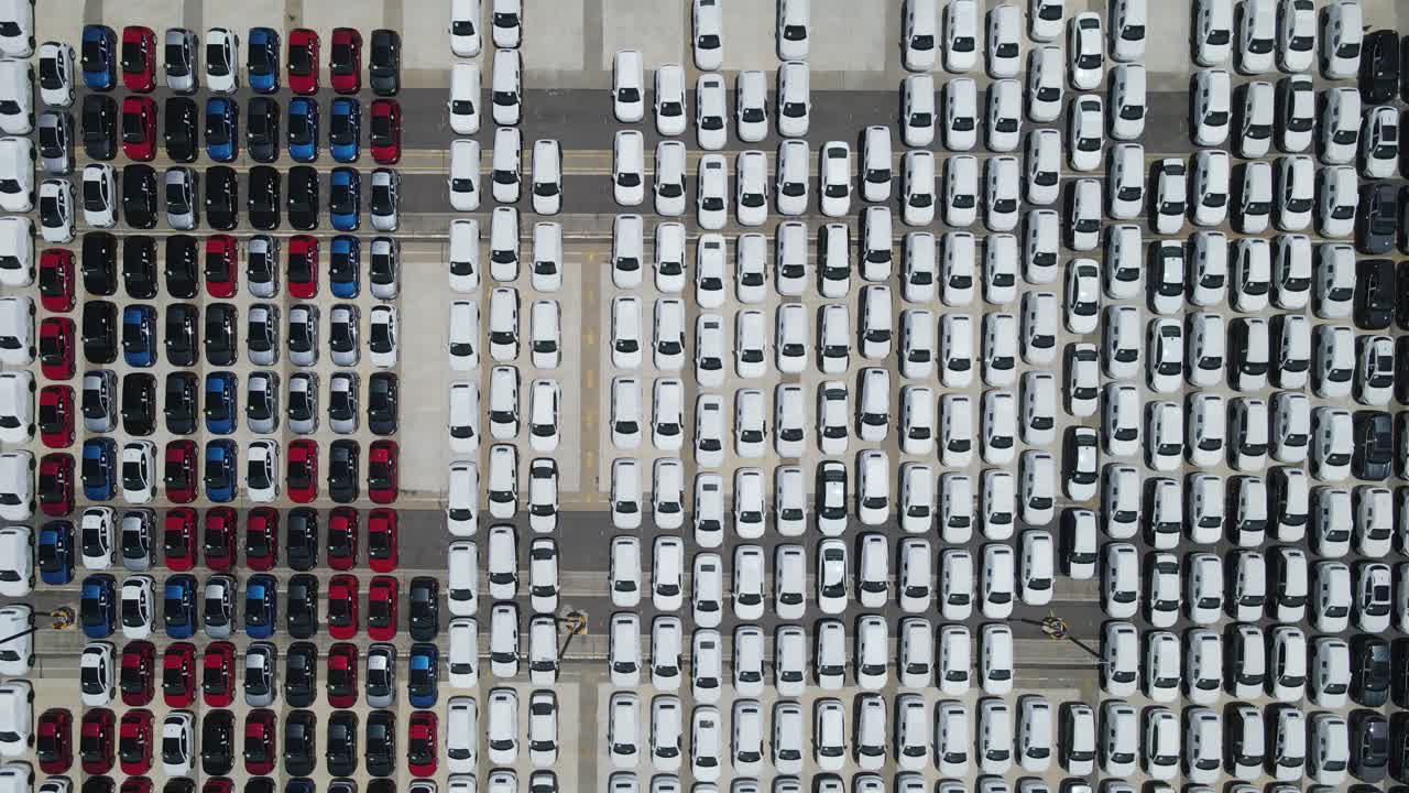 Camera ascends over a vast lot filled with neatly parked cars in white, red, black, and blue