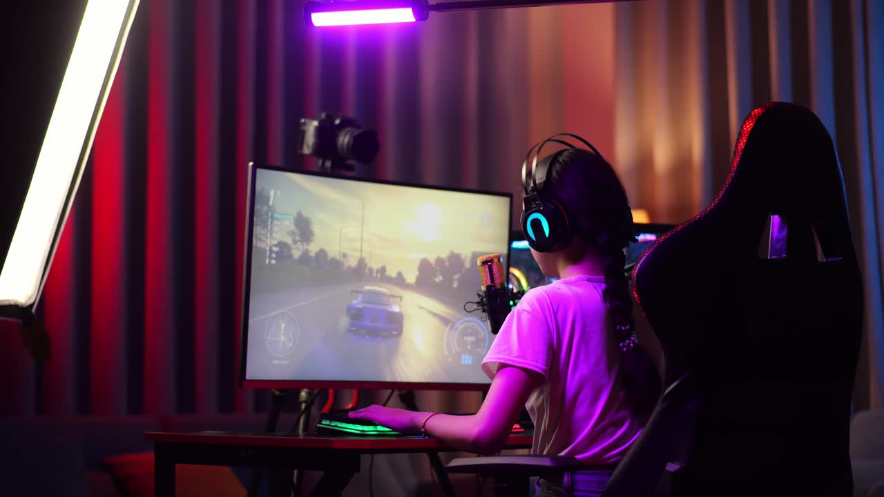 vista trasera de una chica asiática gritando gol y bailando celebrando la victoria en un juego de carreras de coches a través de la red en una computadora personal. videojuego de transmisión en vivo, escritorio iluminado por luz de tira led rgb