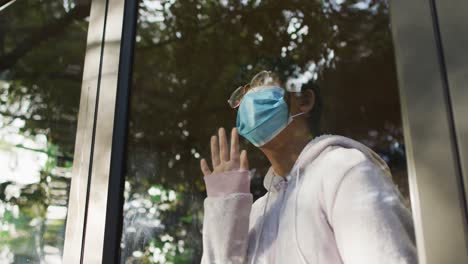 chica asiática con máscara facial y mirando por la ventana