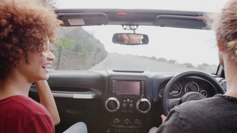una pareja joven conduciendo un coche de alquiler abierto en las vacaciones de verano.
