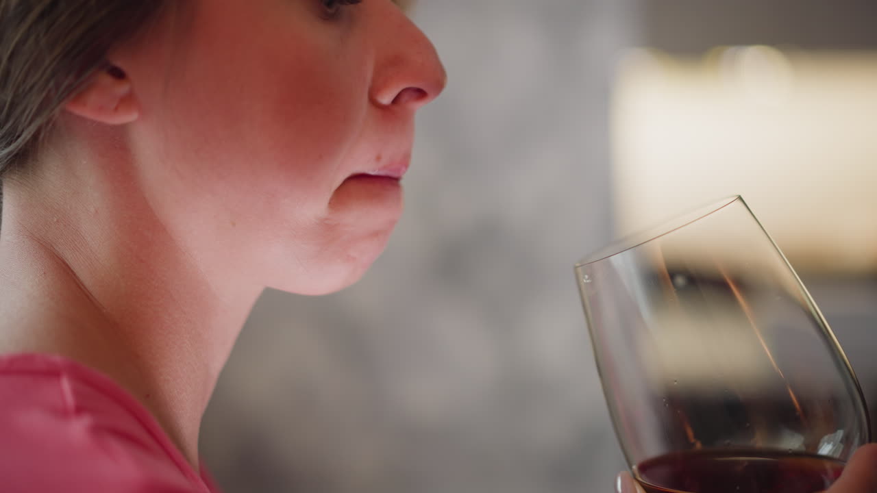 Close up of young adult licking lips while holding cup of fruit juice showing subtle enjoyment moment in cozy indoor setting with soft blurred background