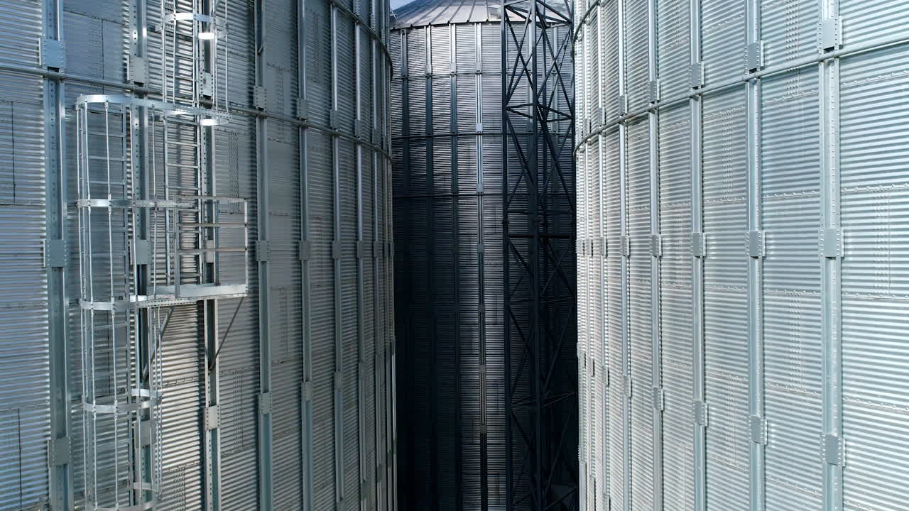 Large metal silo for storing grain. Modern industrial plant. Granary. Silver containers storing agriculture crop. Grain elevators on nature background. Close-up. Motion up.