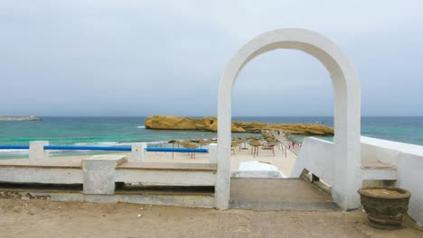 white arch and fence on beach with umbrellas and rocks near the sea