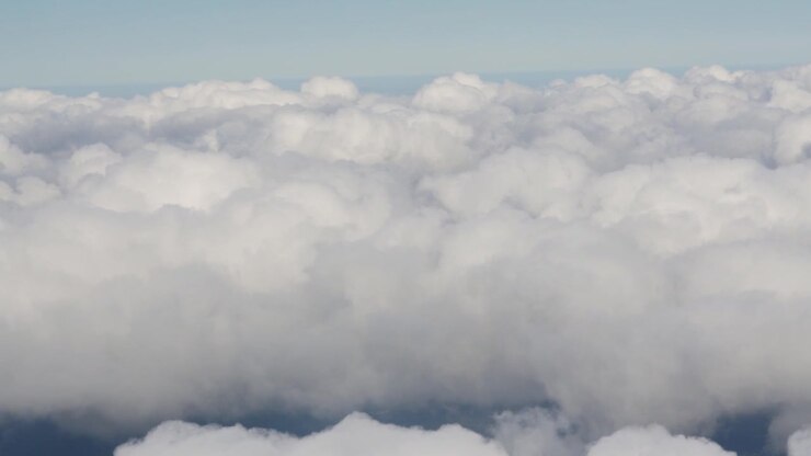 Clouds cover the sky as seen from an aircraft. White, fluffy formations are visible from different angles. The view highlights the texture and movement of the clouds.