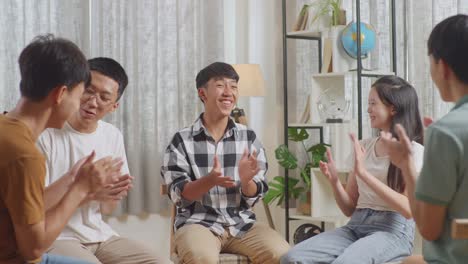 asian teen group sitting in chairs forming a circle discussing at home. celebrating, applause or audience clapping hands after a boy in plaid shirt giving speech