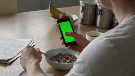 hombre usando un teléfono inteligente con pantalla verde y tomando el desayuno