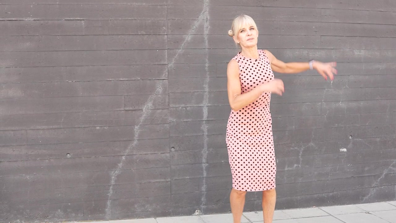 Una donna con un vestito a pois rosa cammina accanto a un muro di mattoni in città.