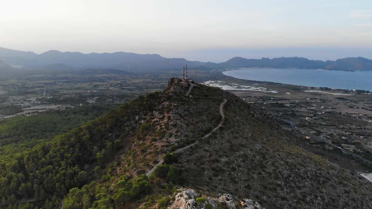 Aerial Over Ridge Line On Forested Hill With Mountains And Lake In Background