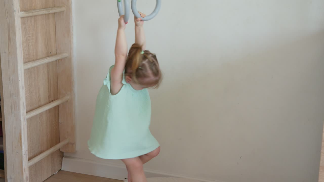 Bambina che gioca e si appende agli anelli da ginnastica al chiuso