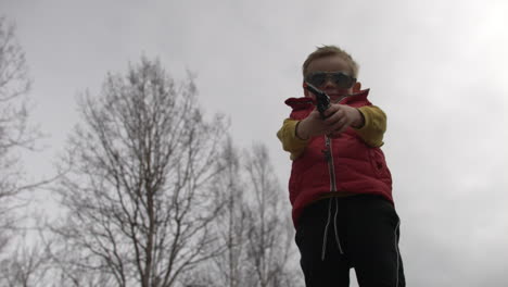 Blonde-Caucasian-boy-points-toy-gun-at-camera,-slow-motion