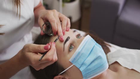 caucasian woman wearing face mask lying down having eyebrows dyed